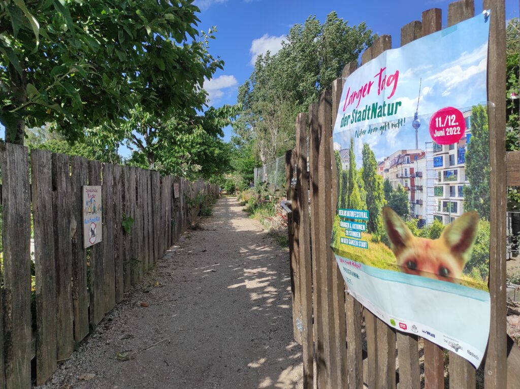 Foto: Das Gartentor der Laskerwiese ist geöffnet. Am Tor hängt ein Plakat mir der Aufschrift Langer Tag der Stadtnatur